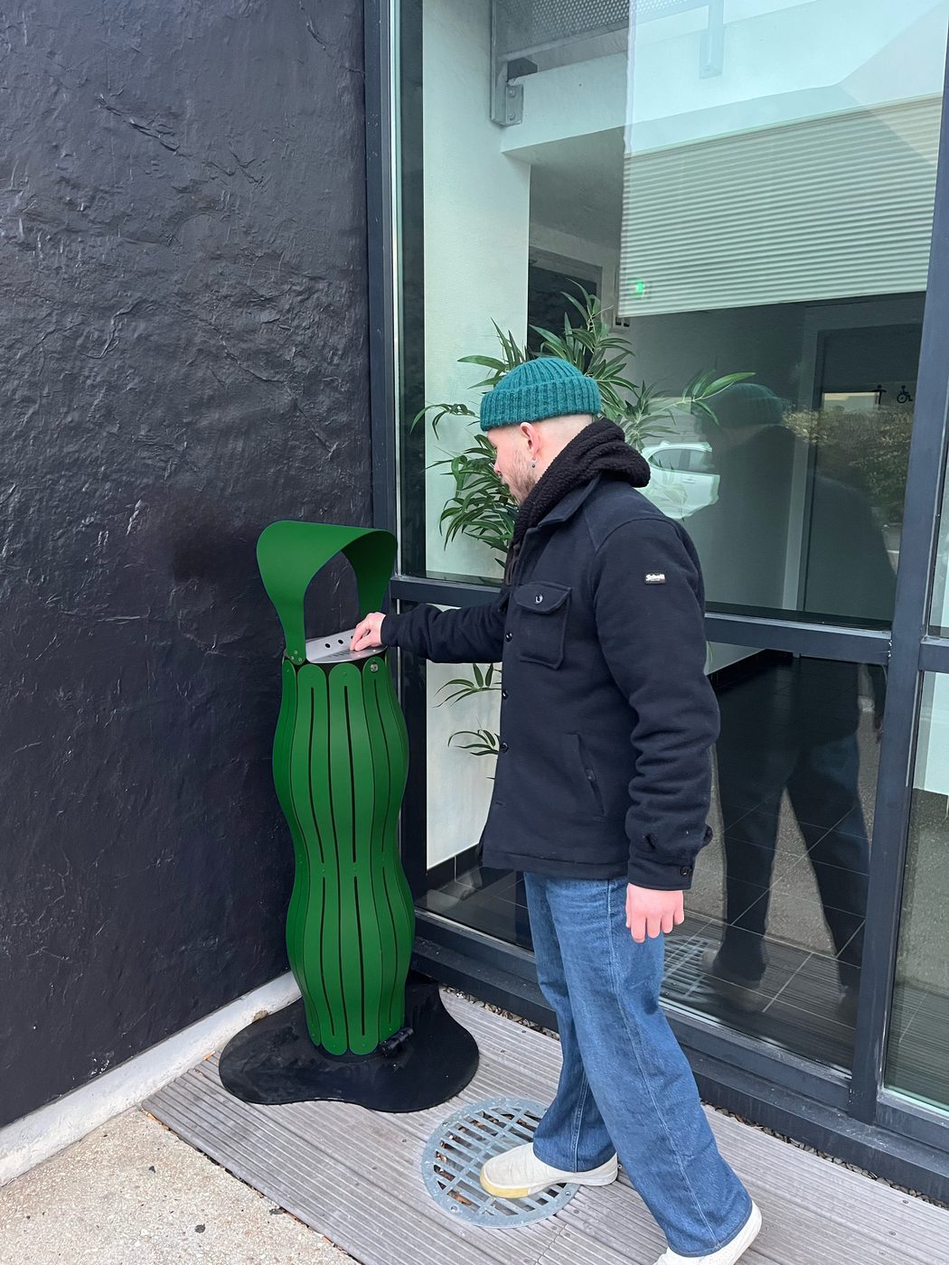 Utilisateur éteignant son mégot sur la coiffe d'un cendrier Moss Green à l'entrée d'un bâtiment